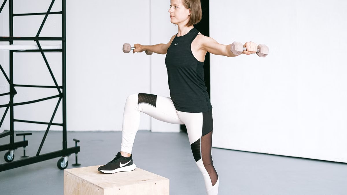 Woman performing fitness exercise with dumbbells in a gym setting, showcasing strength and balance.